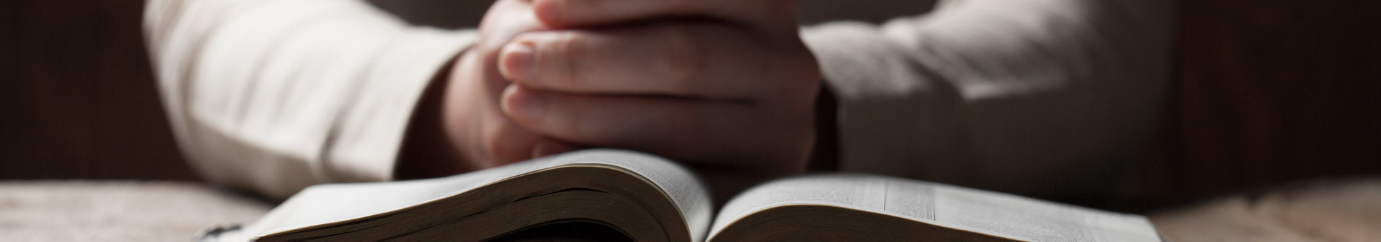 Hands folded in prayer over an open Bible